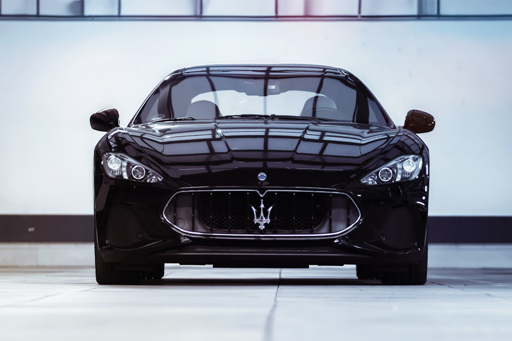 A black Maserati parked indoors with a white wall behind it.